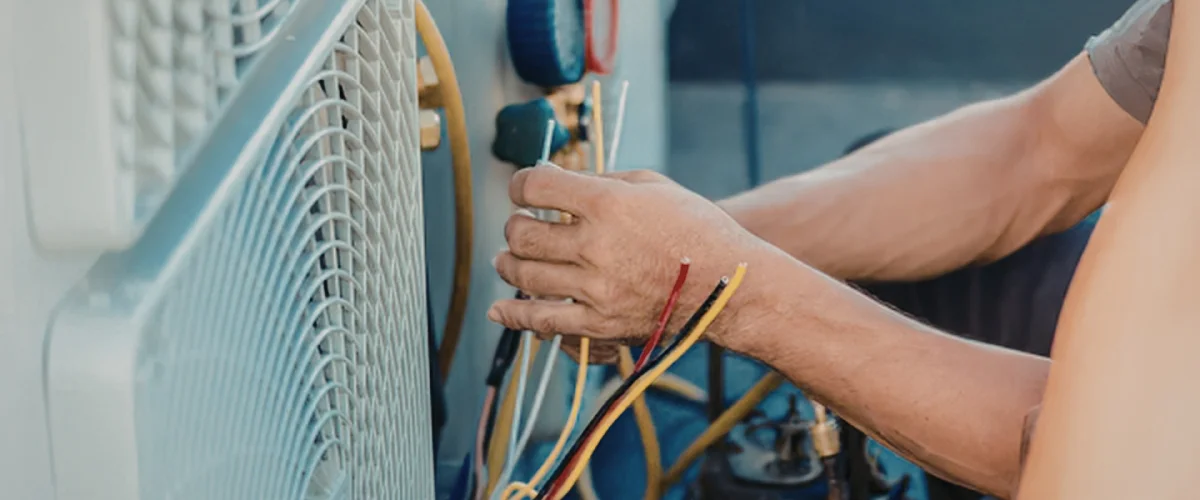 A technician's hands connect colorful electrical wires to an outdoor AC unit during maintenance.