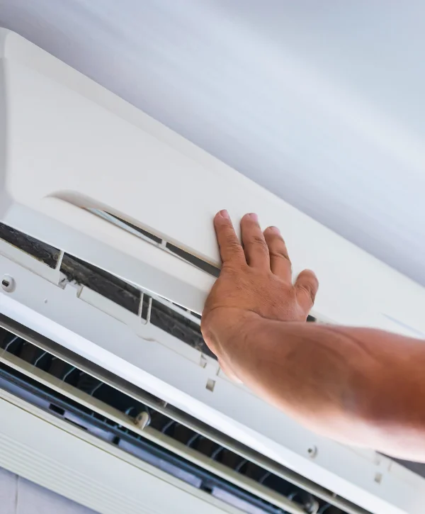 A hand is shown opening the front panel of a dirty wall-mounted air conditioner unit to reveal the dusty filter.