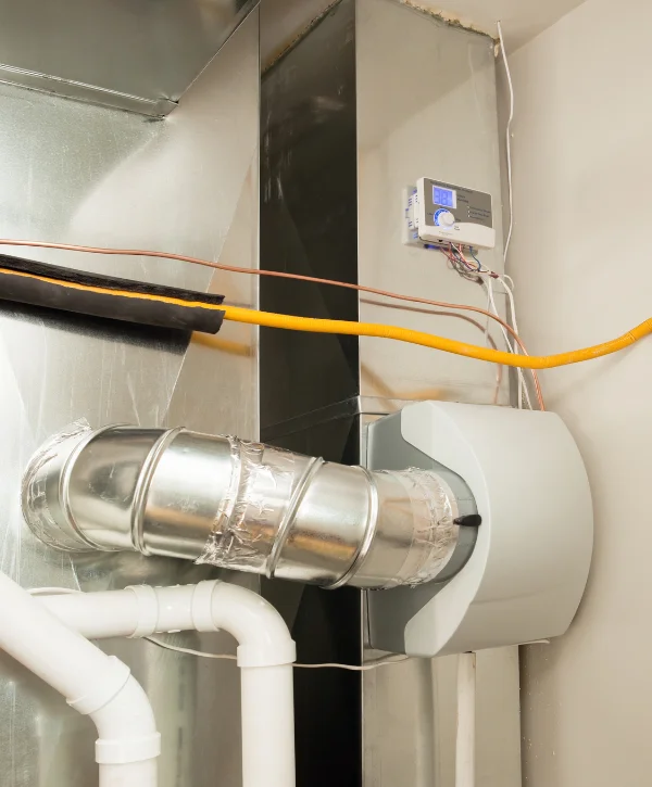 A home furnace humidifier system with gray rectangular unit, silver ducting, white pipes, and control panel.