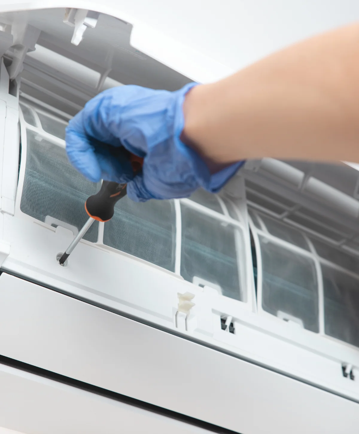 A close-up of a person's hands using a screwdriver to open a white wall-mounted air conditioner unit for maintenance.