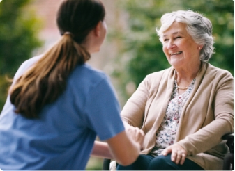 Carer sitting with an elderly woman and holding her hands in an aged care setting