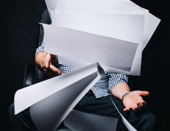 Person holding a large disordered armful of loose printed paper