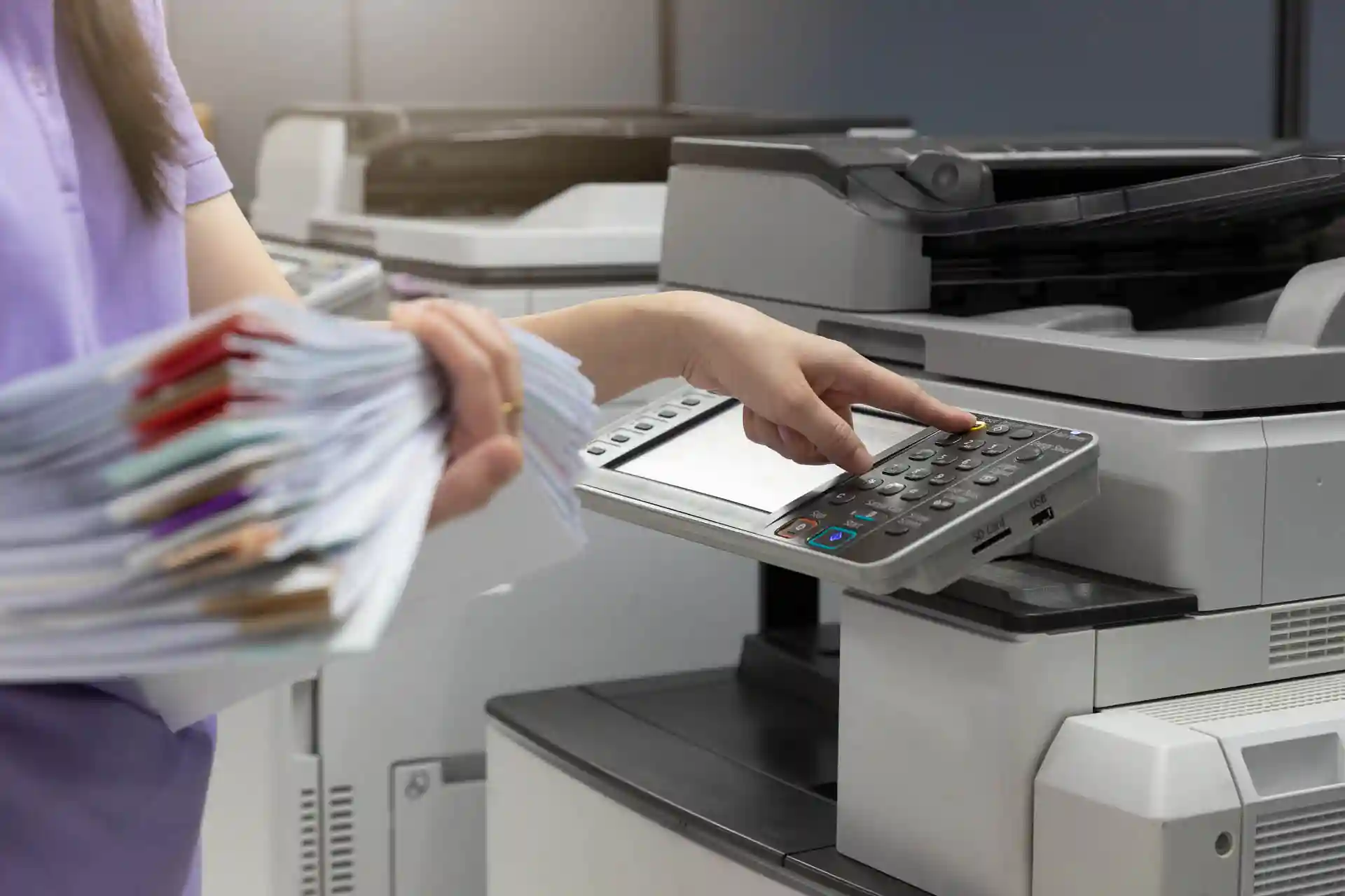 Person loading a large stack of paper into the document feeder of an office multifunction printer