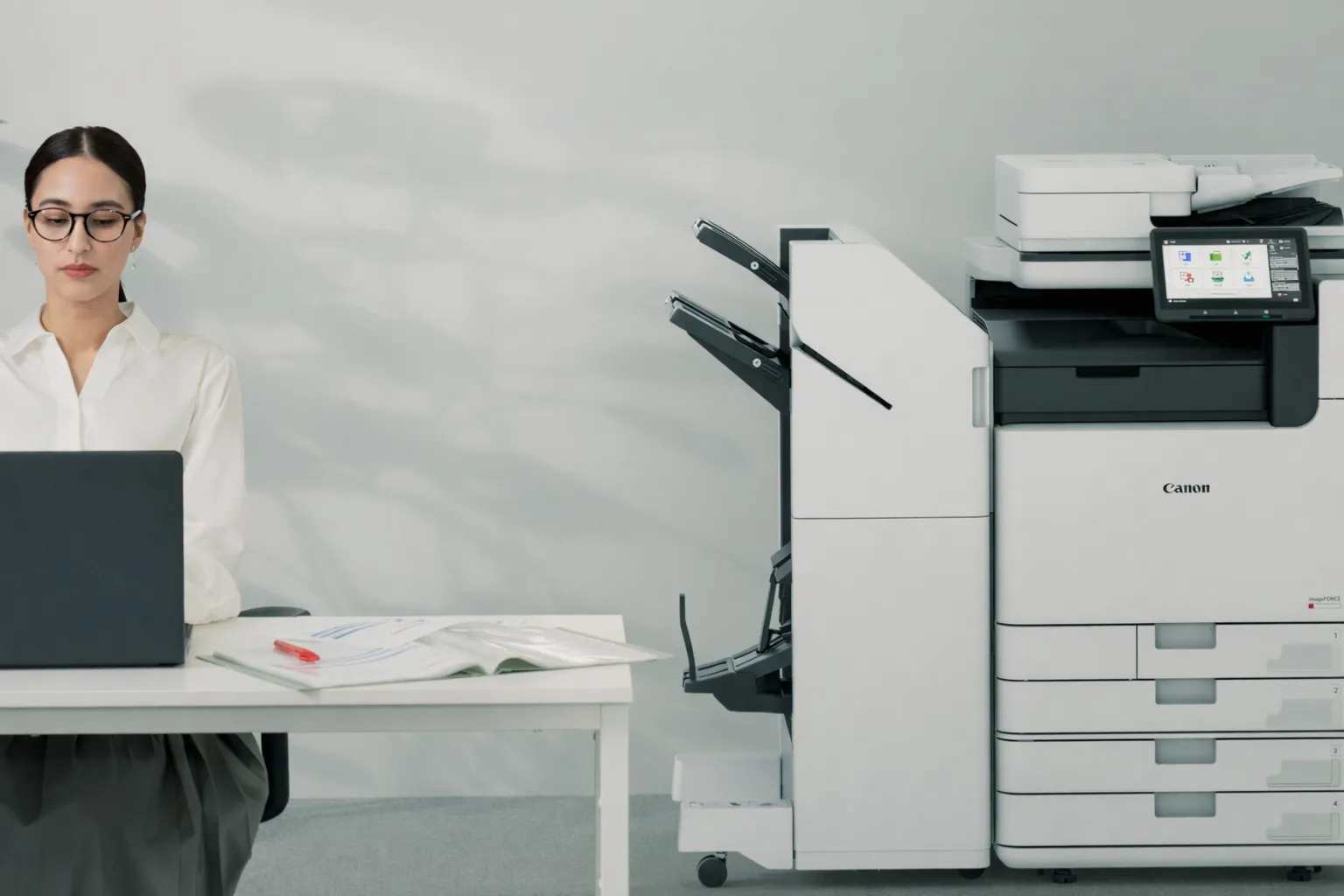 Woman working at a desk beside a Canon multifunction printer in an office
