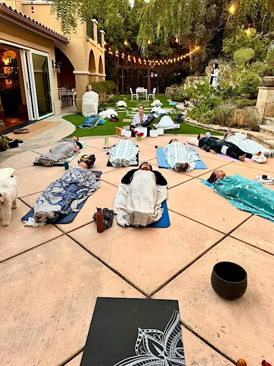 Guests resting on mats under string lights at an evening sound healing