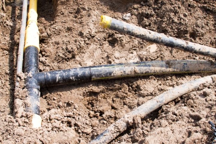 Partially buried utility pipes exposed during landscaping, risking accidental plumbing damage.