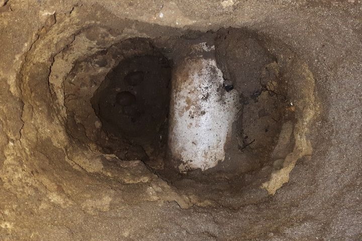 A white pipe visible in a freshly dug dirt hole, vulnerable to plumbing damage.