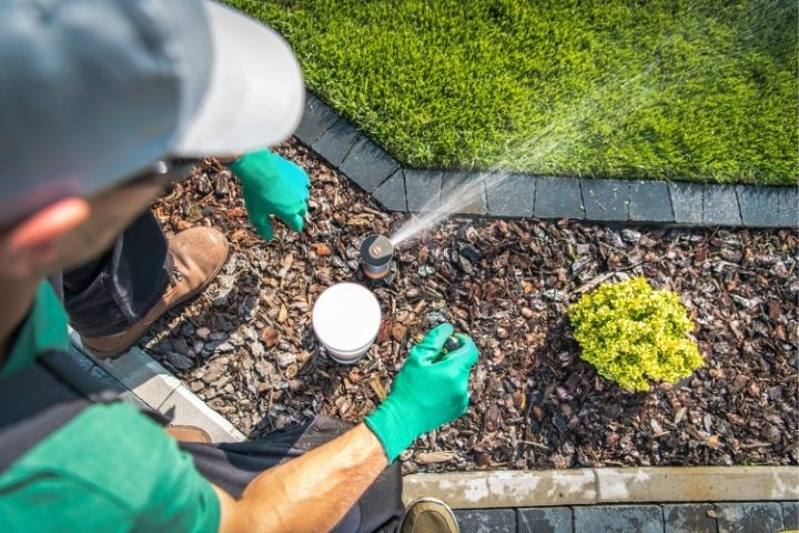 plumber adjusting a garden sprinkler head to prevent unexpected plumbing issues.