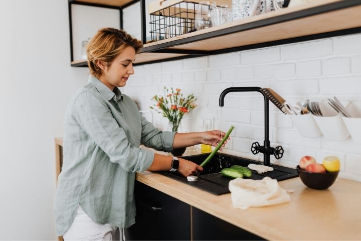 A homeowner using a kitchen sink, maintaining fixtures before calling a plumbing service near me.