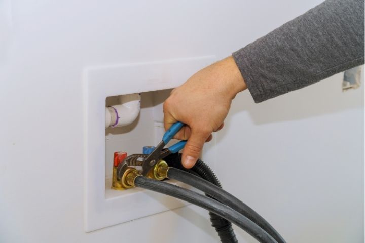 A plumber connecting a hose to a water valve for washing machine plumbing.