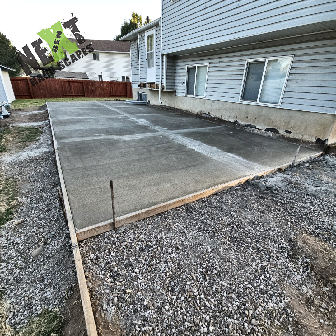 Concrete is freshly poured with a finishing machine smoothing the surface of the patio area next to the house.
