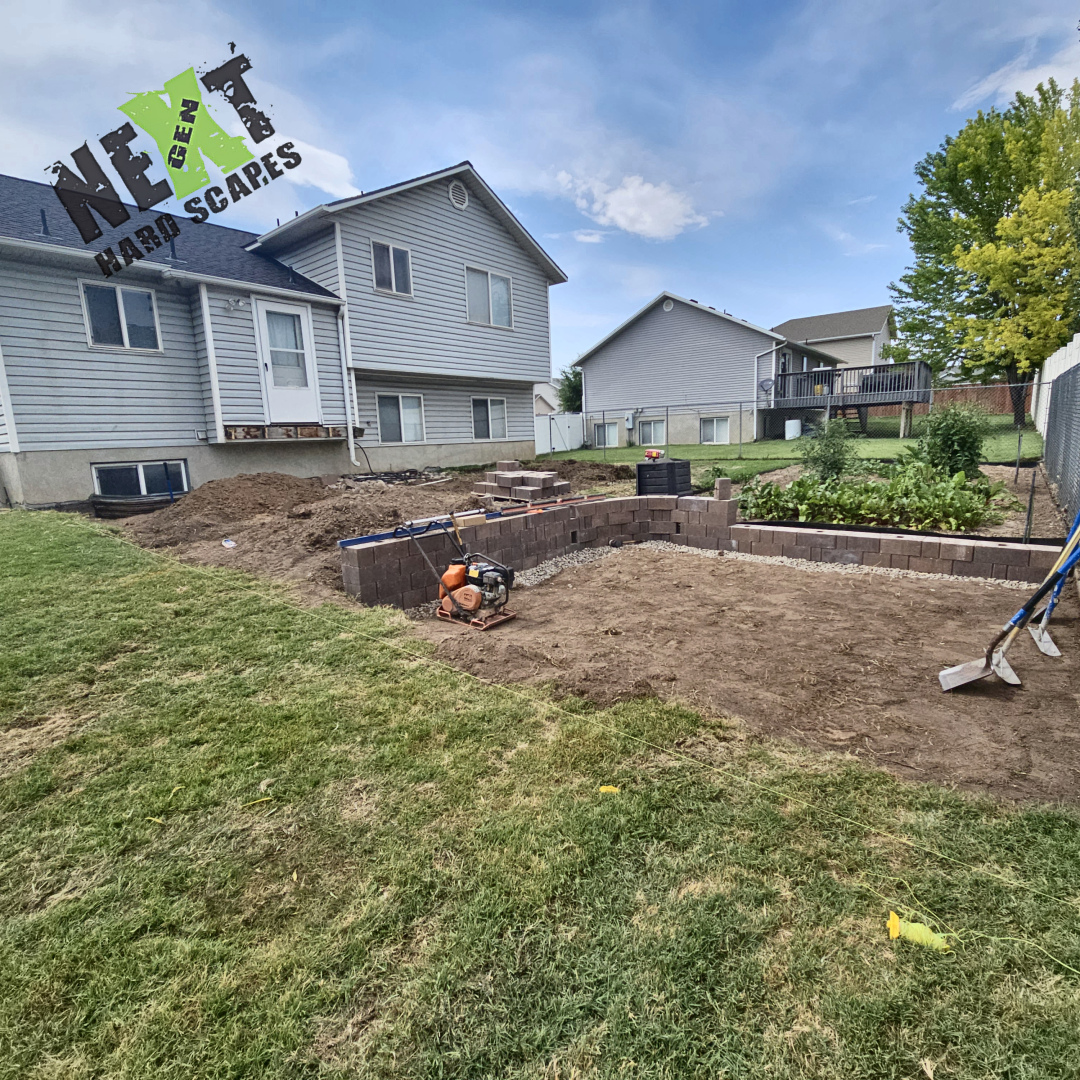 A partial retaining wall is built forming the boundary of the future step-down paver patio beside the garden area.