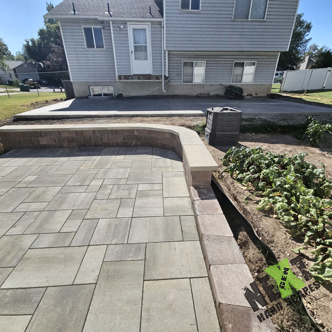 View showing both the cured concrete patio and the adjacent paver patio with retaining wall and garden in the background.