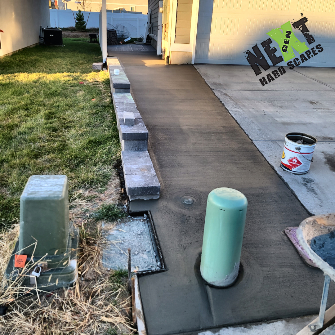 Closer angle showing the retaining wall built with variously colored pavers and the freshly finished concrete driveway beside it.