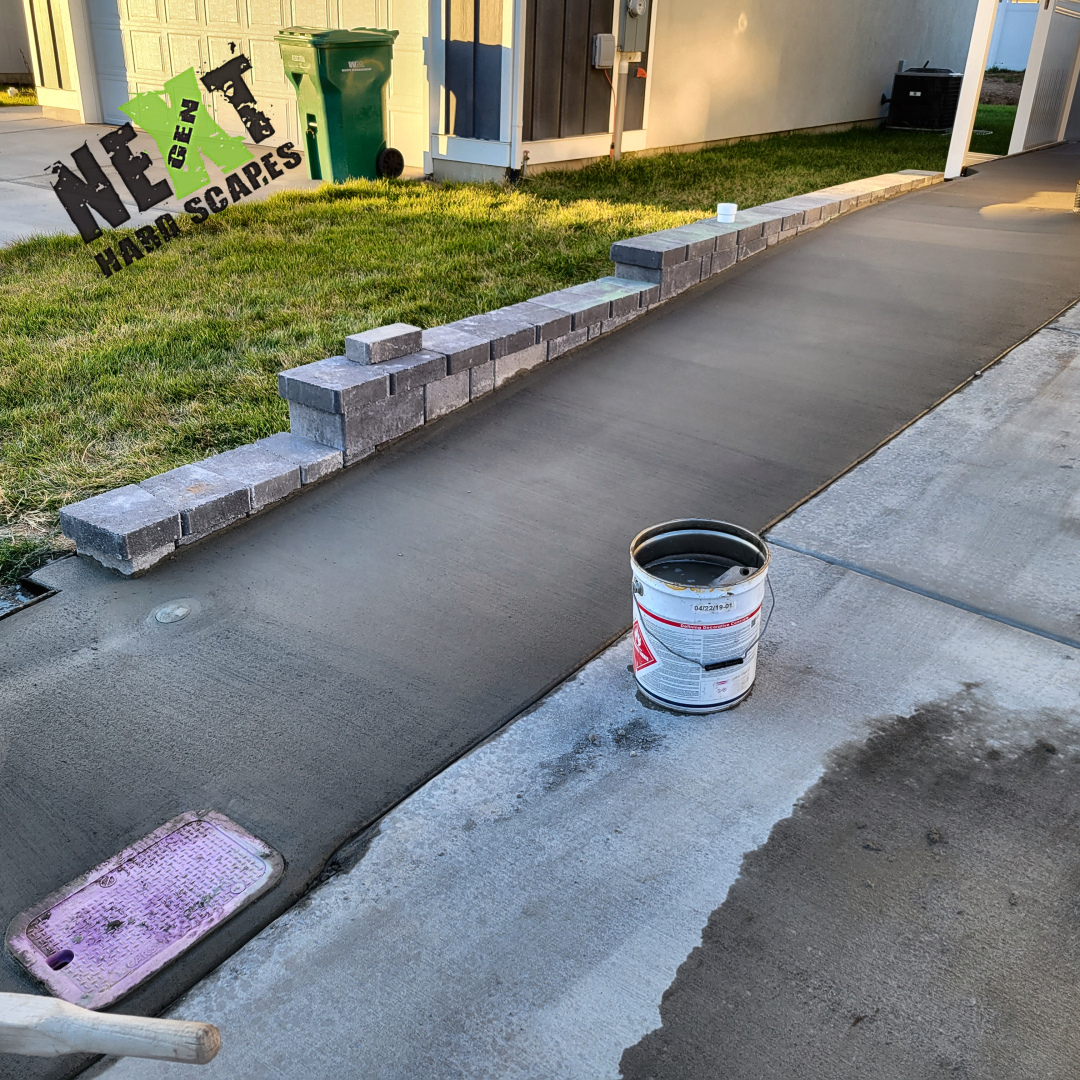 End section of the narrow driveway showing the retaining wall step-down and the new concrete surface bordered by grass and existing concrete driveway.