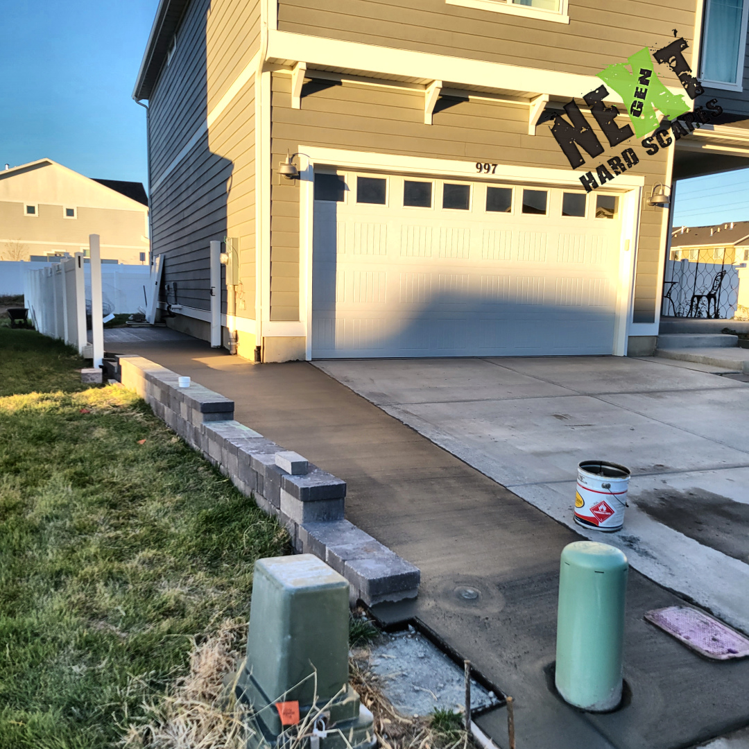 Wide view of the completed tight side driveway with smooth new concrete and a rock paver retaining wall alongside a two-story home.