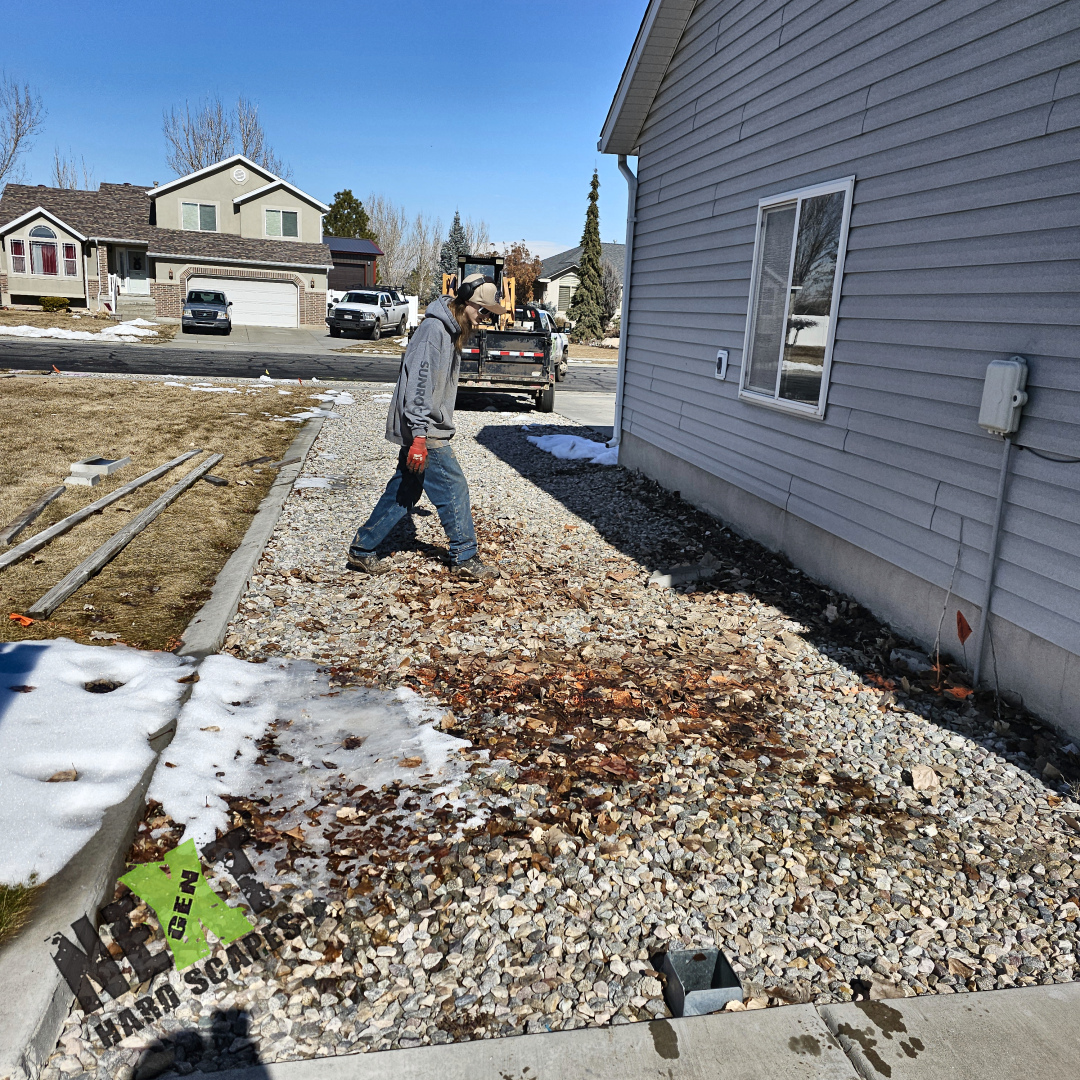 Site preparation underway with the area excavated and base gravel laid along the side of the house, establishing proper subgrade for the new concrete.