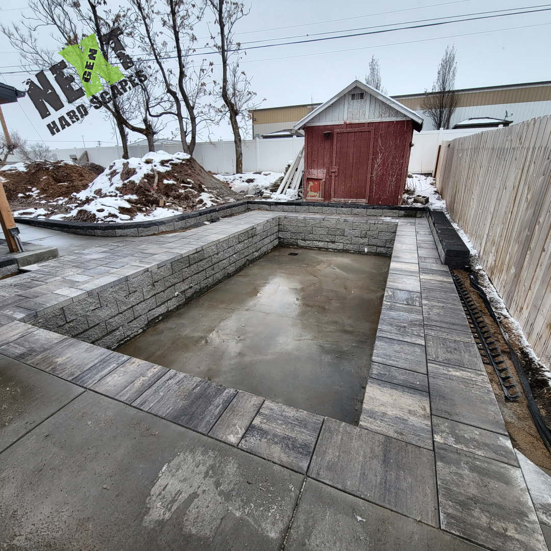 View from covered patio showing concrete slab transition to paver border edging along swim spa retaining wall. View from covered patio showing concrete slab transition to paver border edging along swim spa retaining wall.