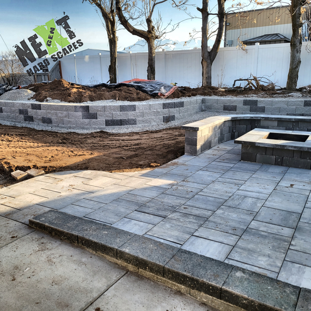 Finished paver patio with fire pit base and curved retaining wall showing uniform block placement and clean mortar joints. Finished paver patio with fire pit base and curved retaining wall showing uniform block placement and clean mortar joints.