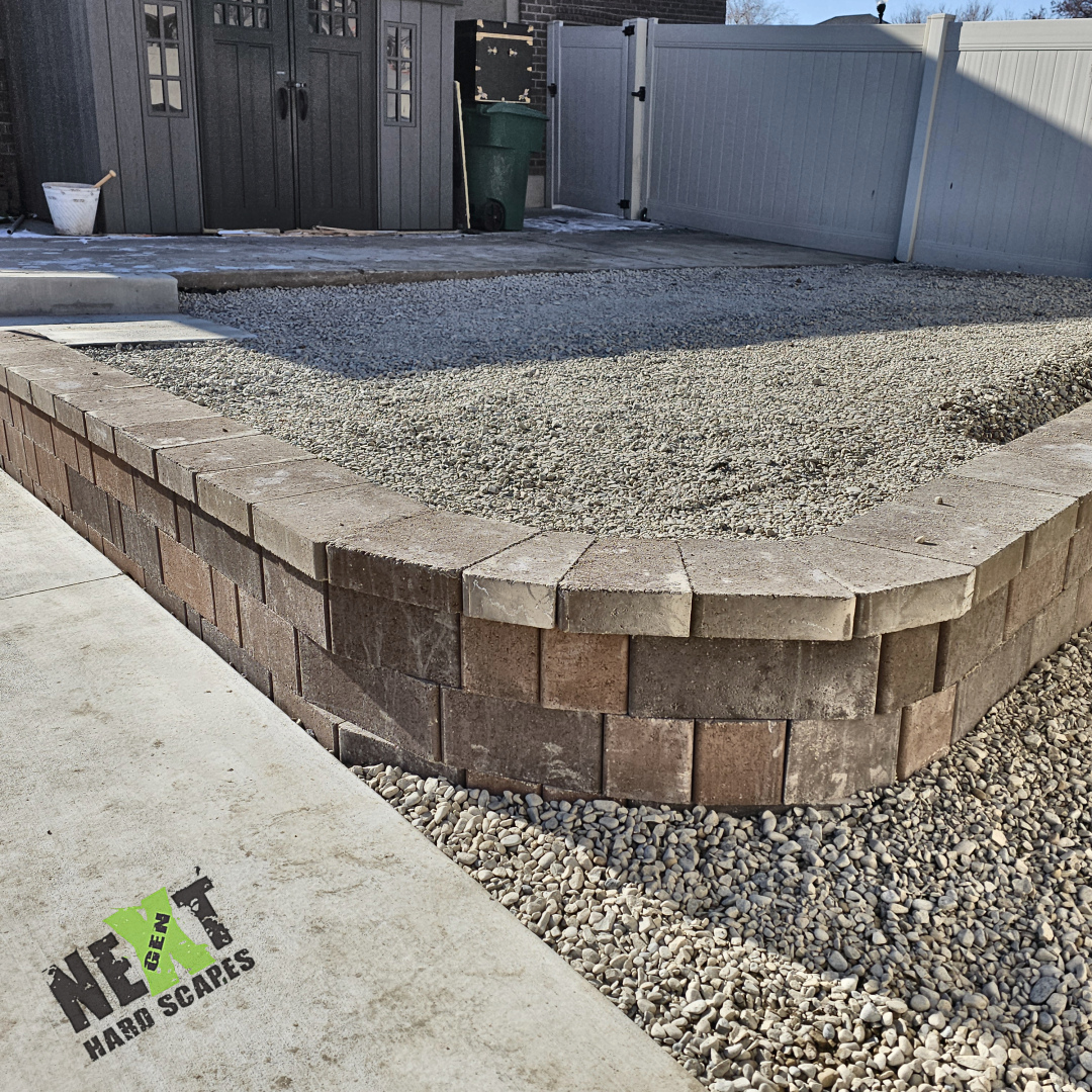 Curved section of the retaining wall with capstones aligned and aggregate base compacted inside the raised planting area. Curved section of the retaining wall with capstones aligned and aggregate base compacted inside the raised planting area.