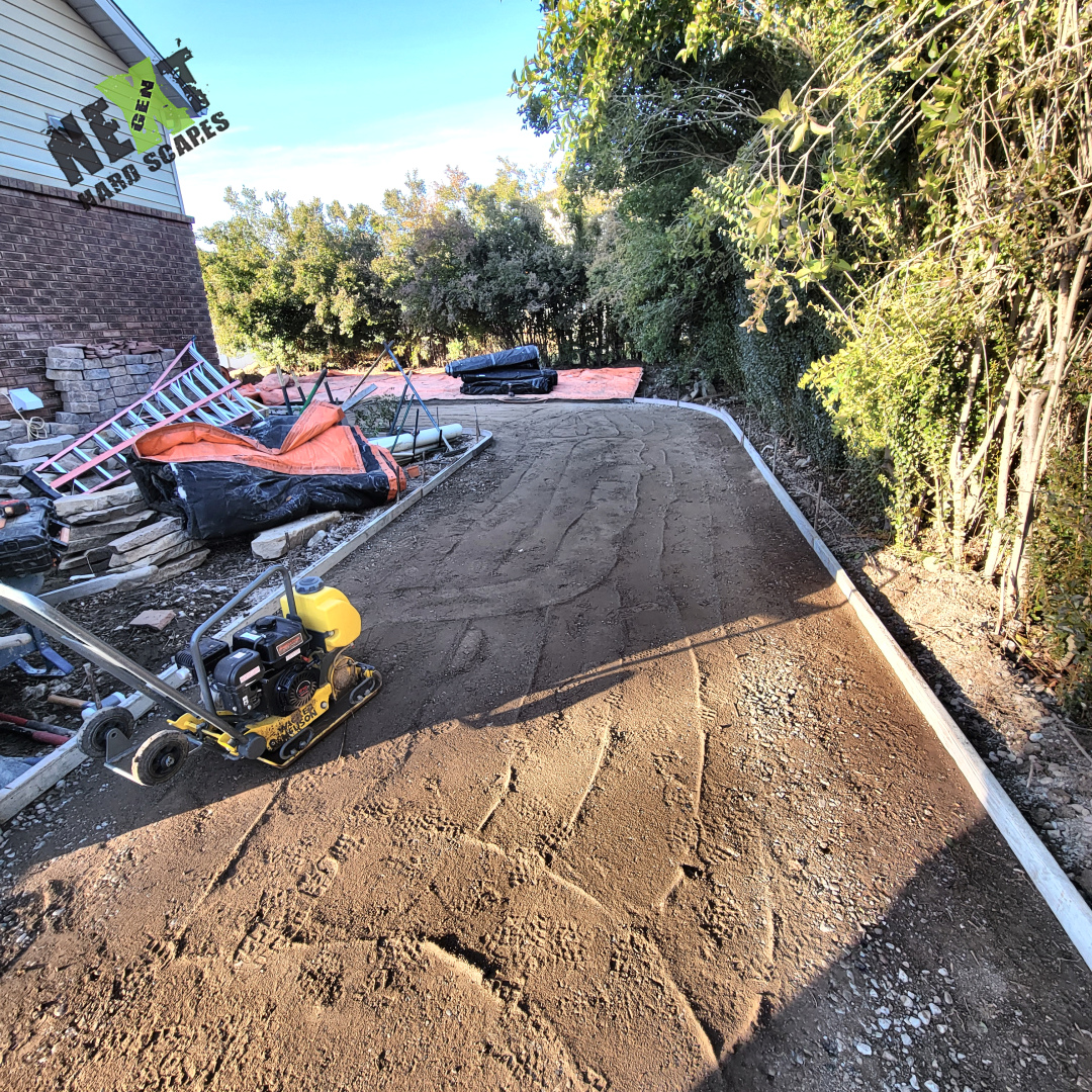Approach path base compacted and leveled with edge forms installed, shown with the plate compactor on site ready for final grading.