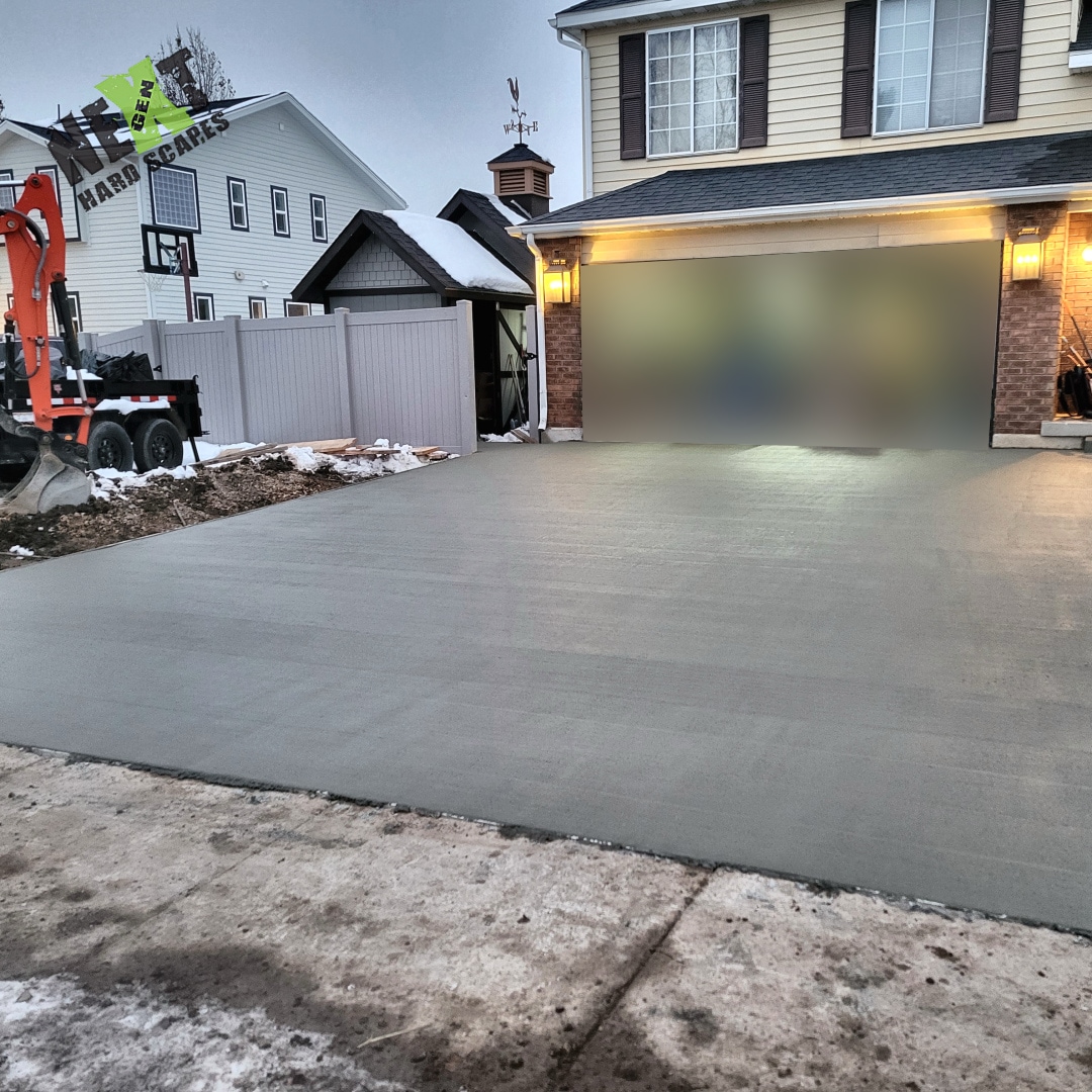 Final front driveway pour completed to a smooth, uniform surface meeting the garage threshold with formed edges intact.