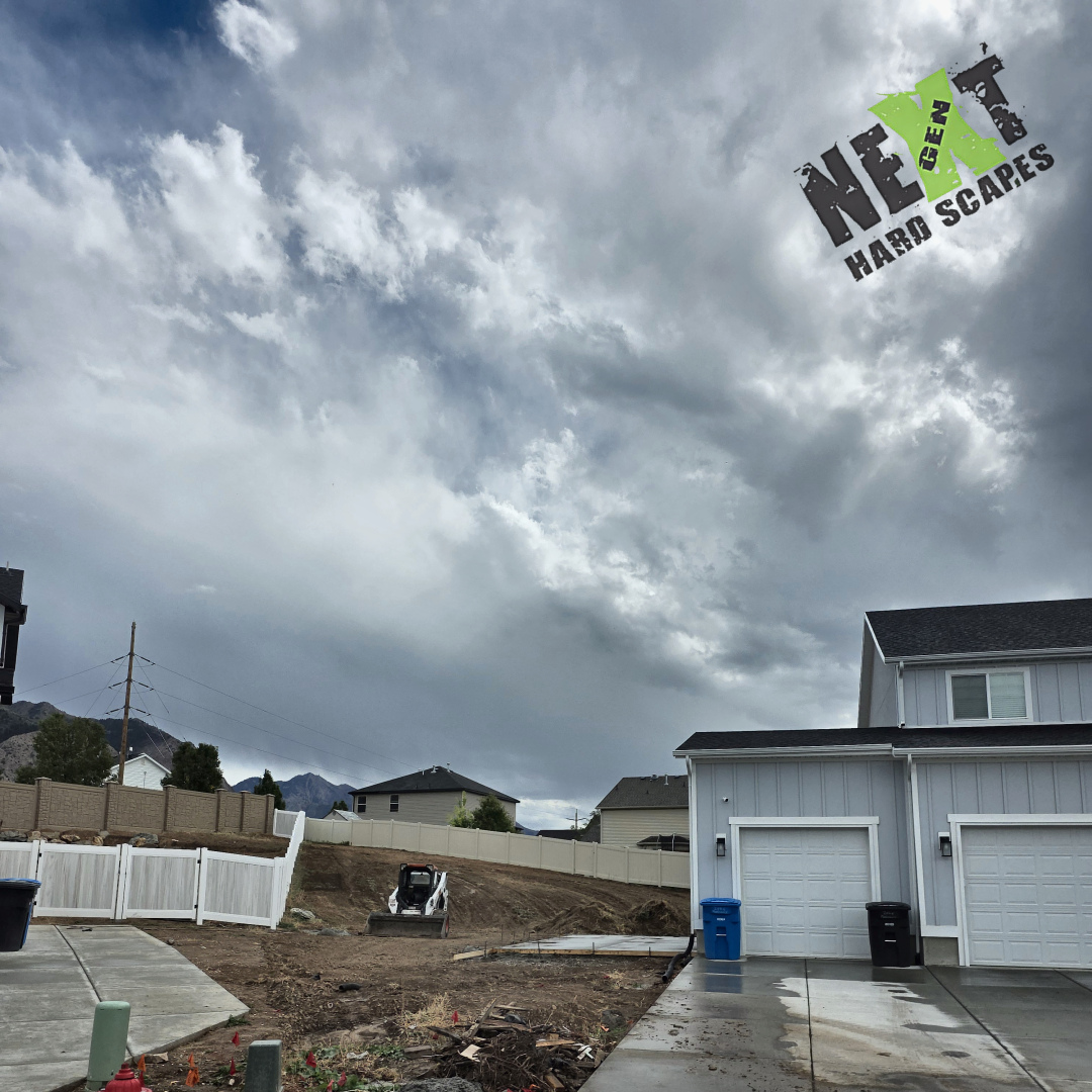 Rough-graded front yard with the skid steer on site and the driveway area cleared and sloped back to the fence ready for base work.