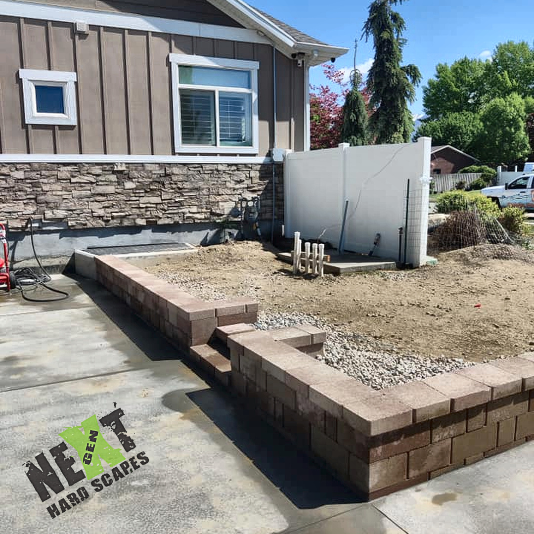 Low retaining wall and cap installed along the pool deck with backfill still loose and plumbing stub-ups exposed behind the wall.