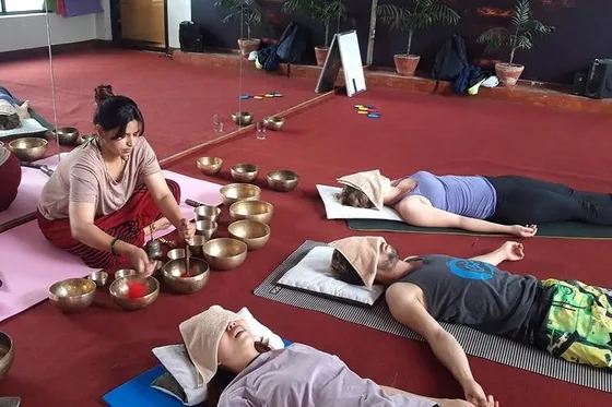 Sound healing practitioner playing brass singing bowls for a group resting on mats during a sound bath.