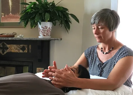 Holistic practitioner giving a calm energy healing session to a client resting on a treatment table.