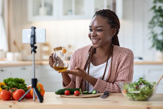Nutrition coach smiling while filming a healthy cooking video on her phone in a bright kitchen.