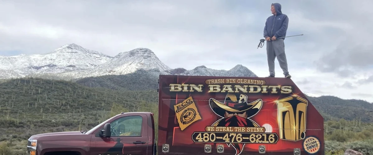 Technician standing on Bin Bandits truck with mountain landscape backdrop Technician standing on Bin Bandits truck with mountain landscape backdrop