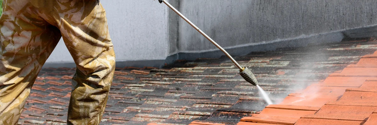 Worker pressure washing clay roof tiles on residential home.