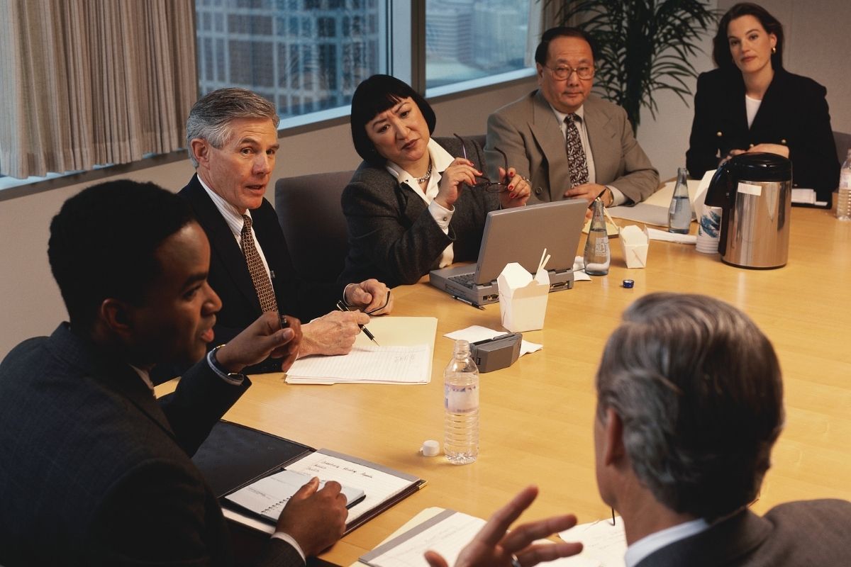 A group of people in a meeting with careful, watchful body language.