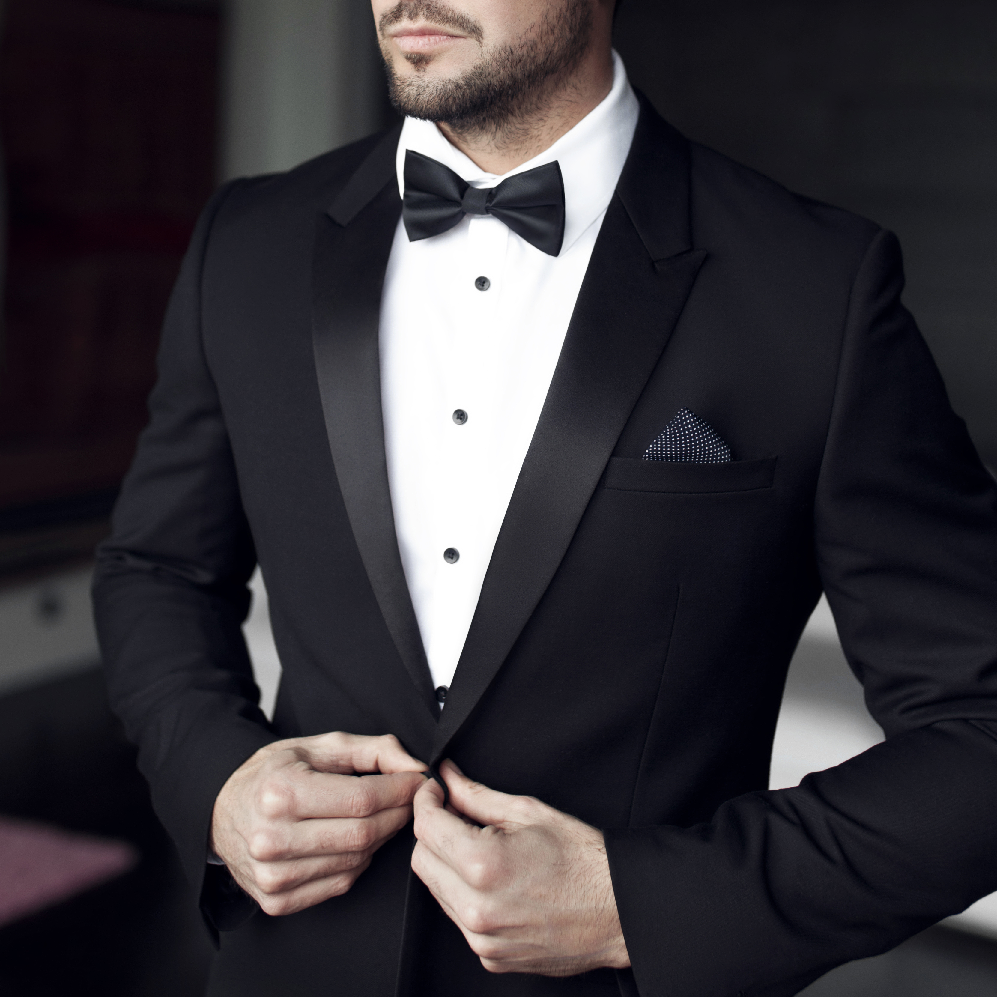 A man in a black tuxedo for a black tie event with a white dress shirt, black bow tie and white pocket square