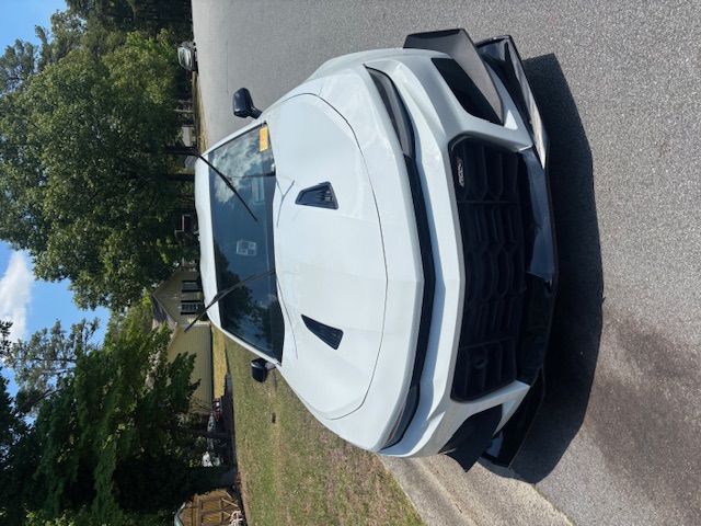 White car cleaned and parked on a street with trees behind