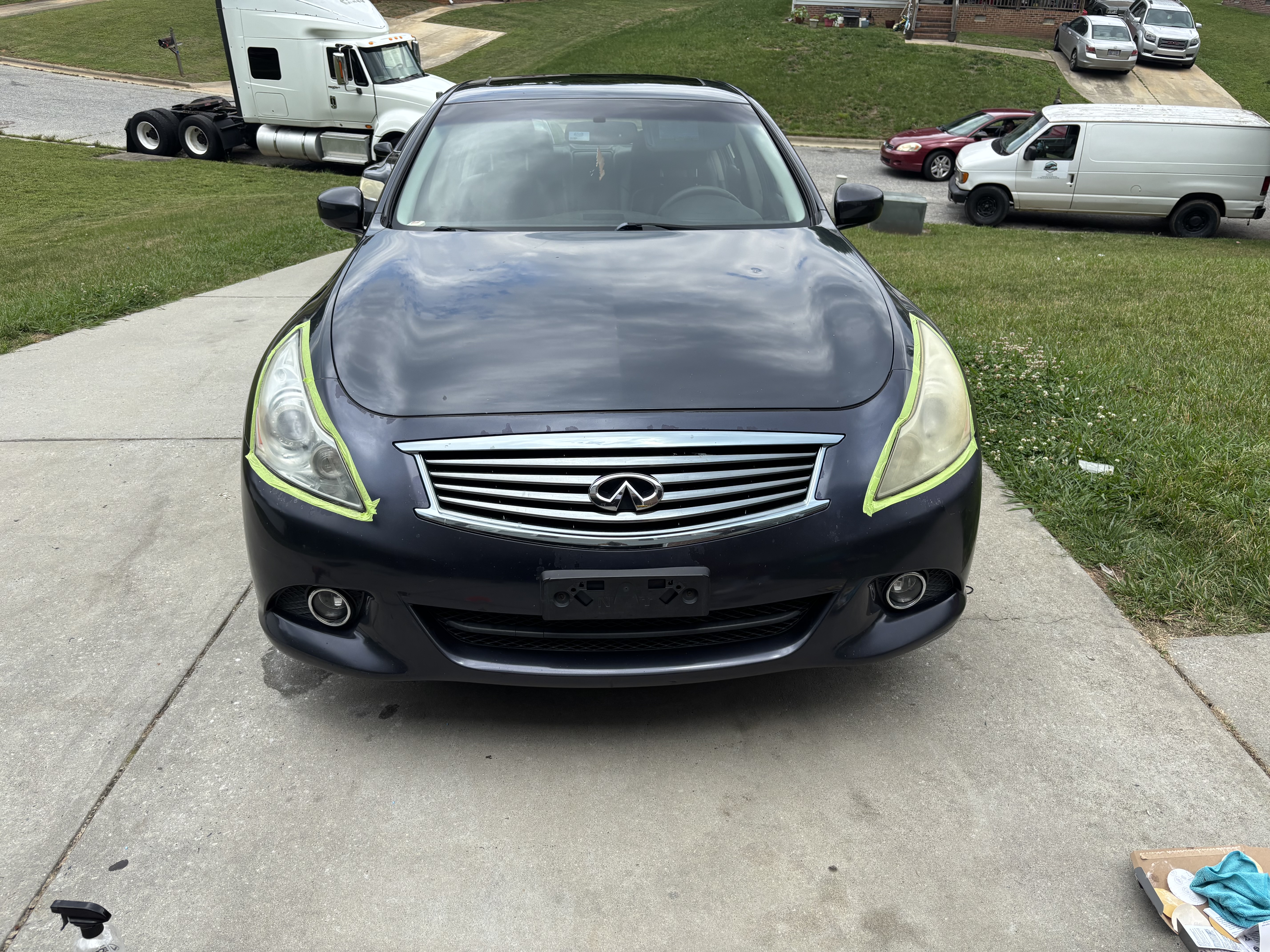 Black car detailed in a driveway with tape on the front