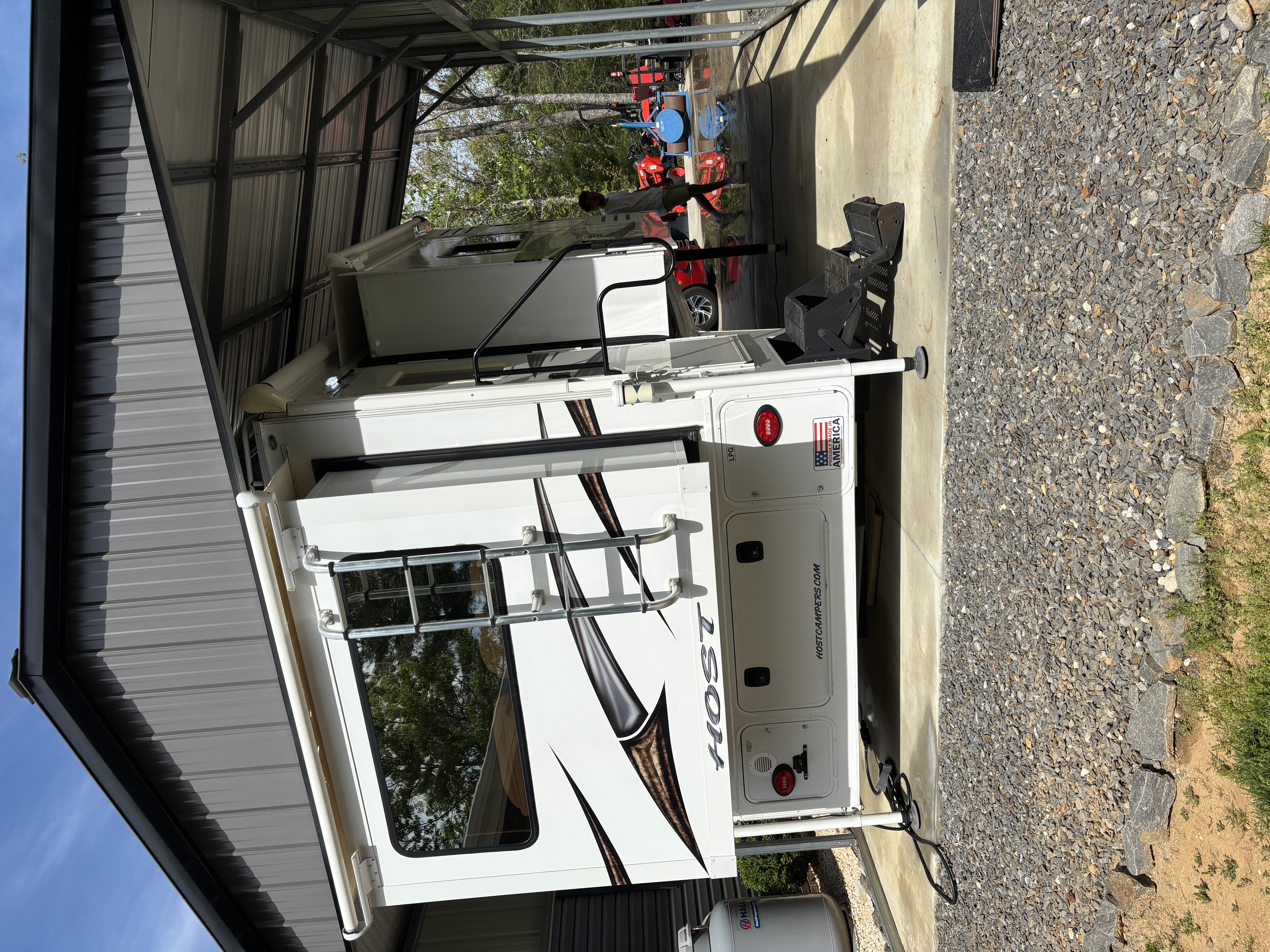 Large white RV with HOST livery detailed under a metal cover — exterior