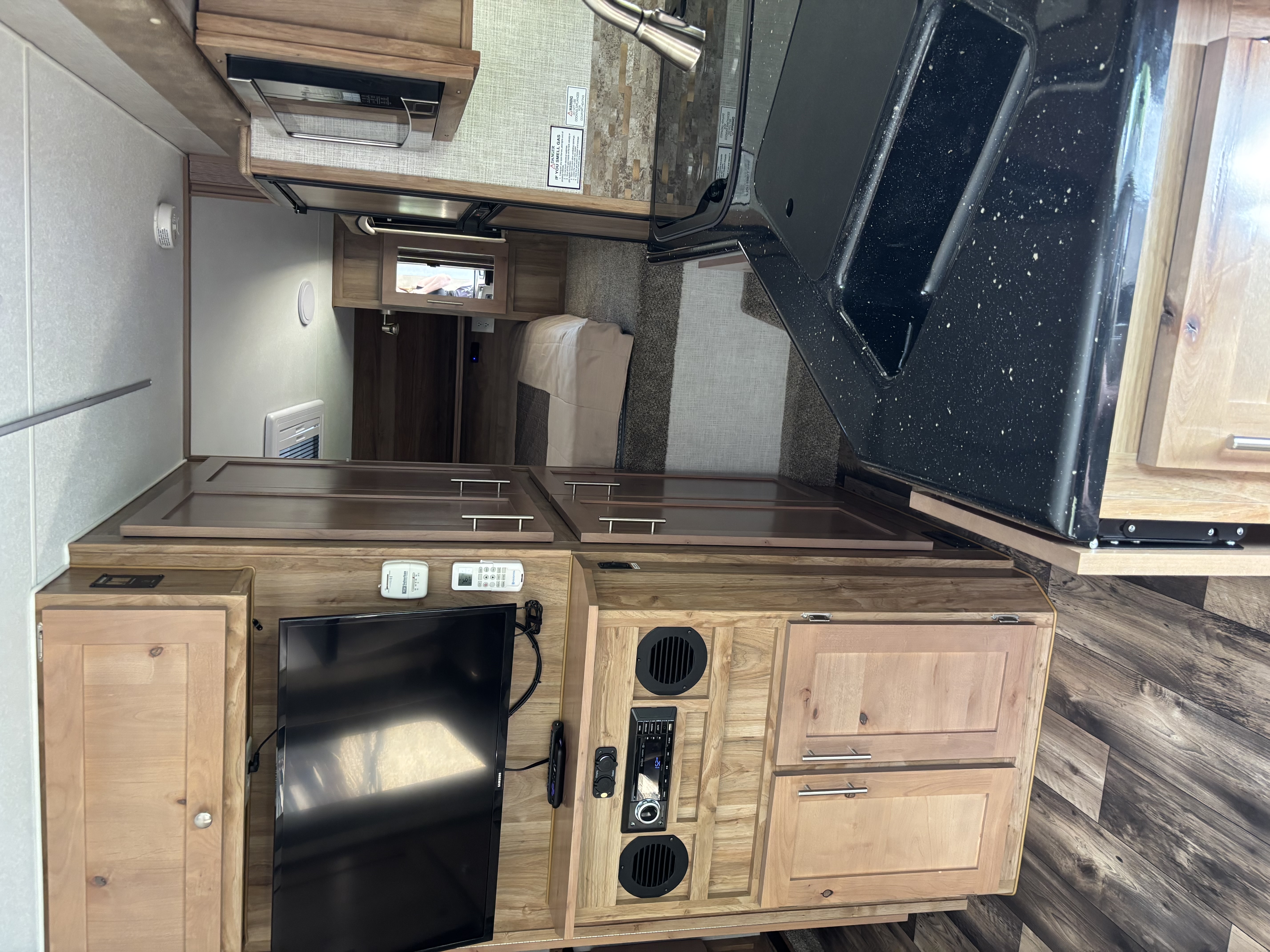 RV interior with clean wooden cabinets, TV, kitchen and bedroom