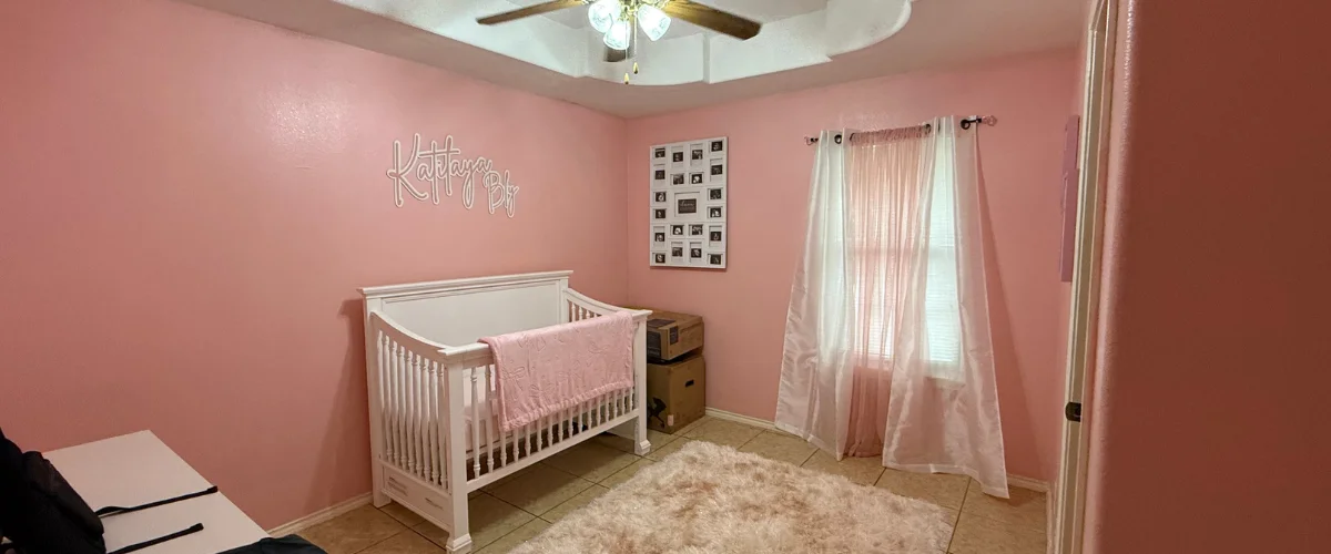A baby's nursery with pink walls, a white crib with a pink blanket, a window with sheer curtains, and a fluffy rug. A baby's nursery with pink walls, a white crib with a pink blanket, a window with sheer curtains, and a fluffy rug.