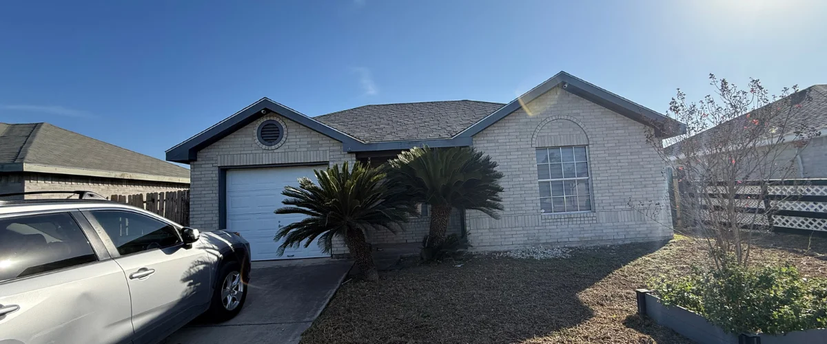 A light brick house with a white garage door, two palm trees, and a silver car parked on a sunny driveway. A light brick house with a white garage door, two palm trees, and a silver car parked on a sunny driveway.