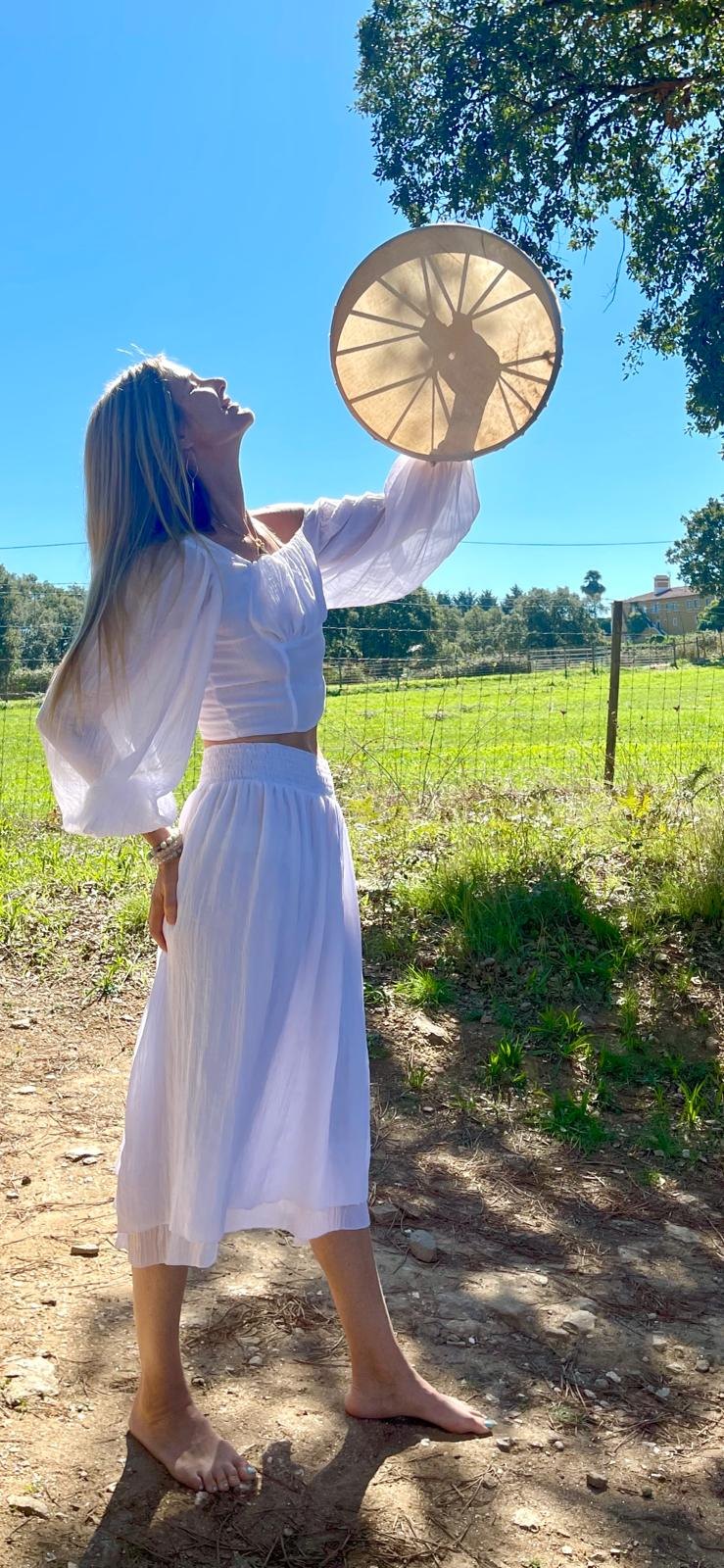 Sandra in white raising a frame drum to the sky