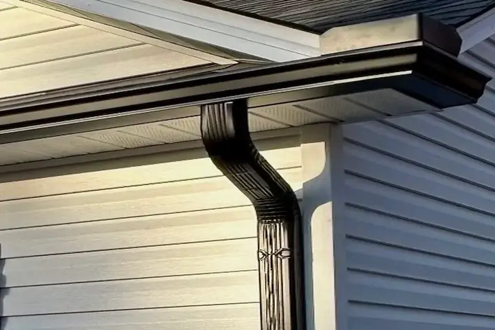 Black gutter and downspout installed against white siding