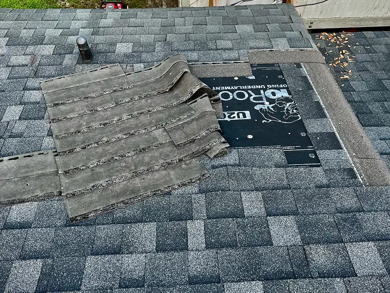 Roof repair area with shingles lifted and underlayment exposed