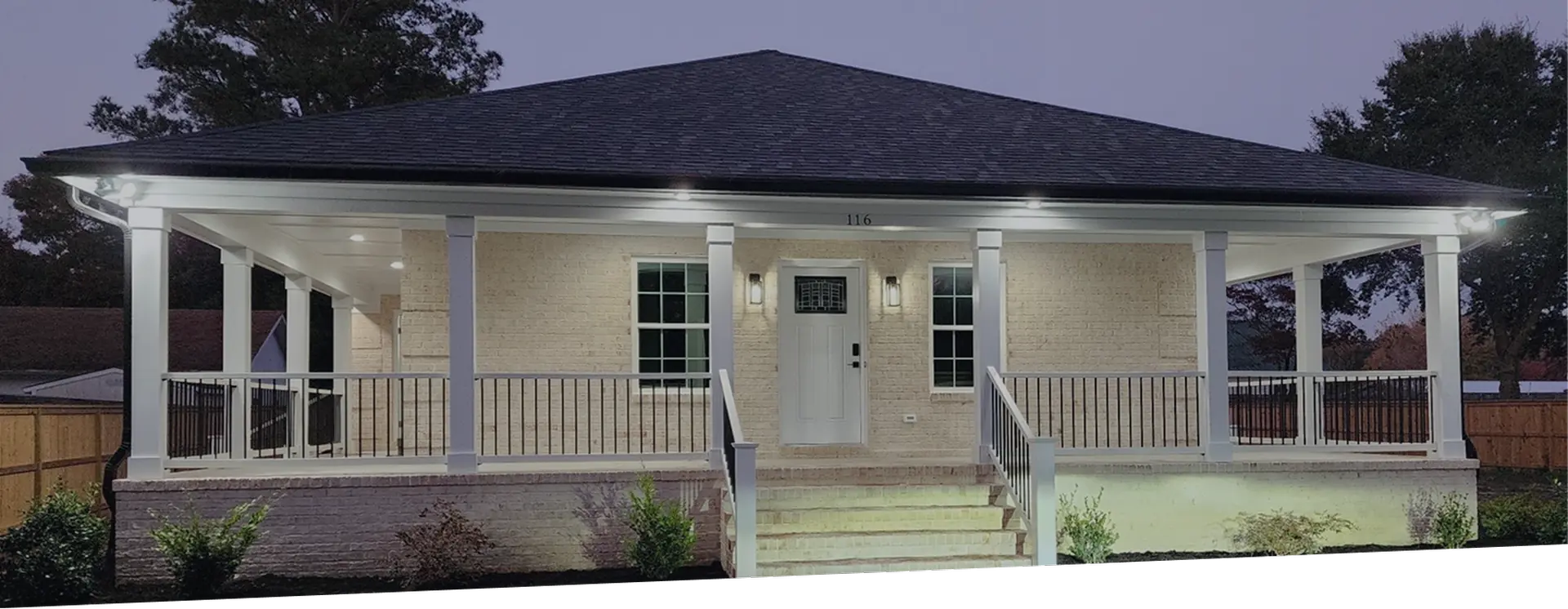 Completed roof and wraparound porch on a one-story home at dusk