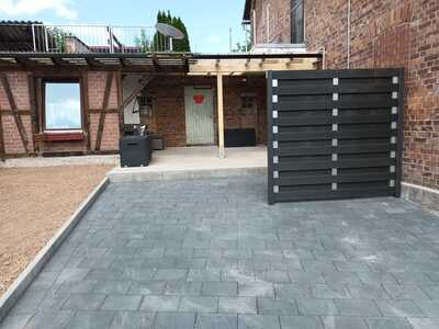 Schwarzer Metallzaun mit Schiebetor auf gepflasterter Einfahrt vor Gebäude