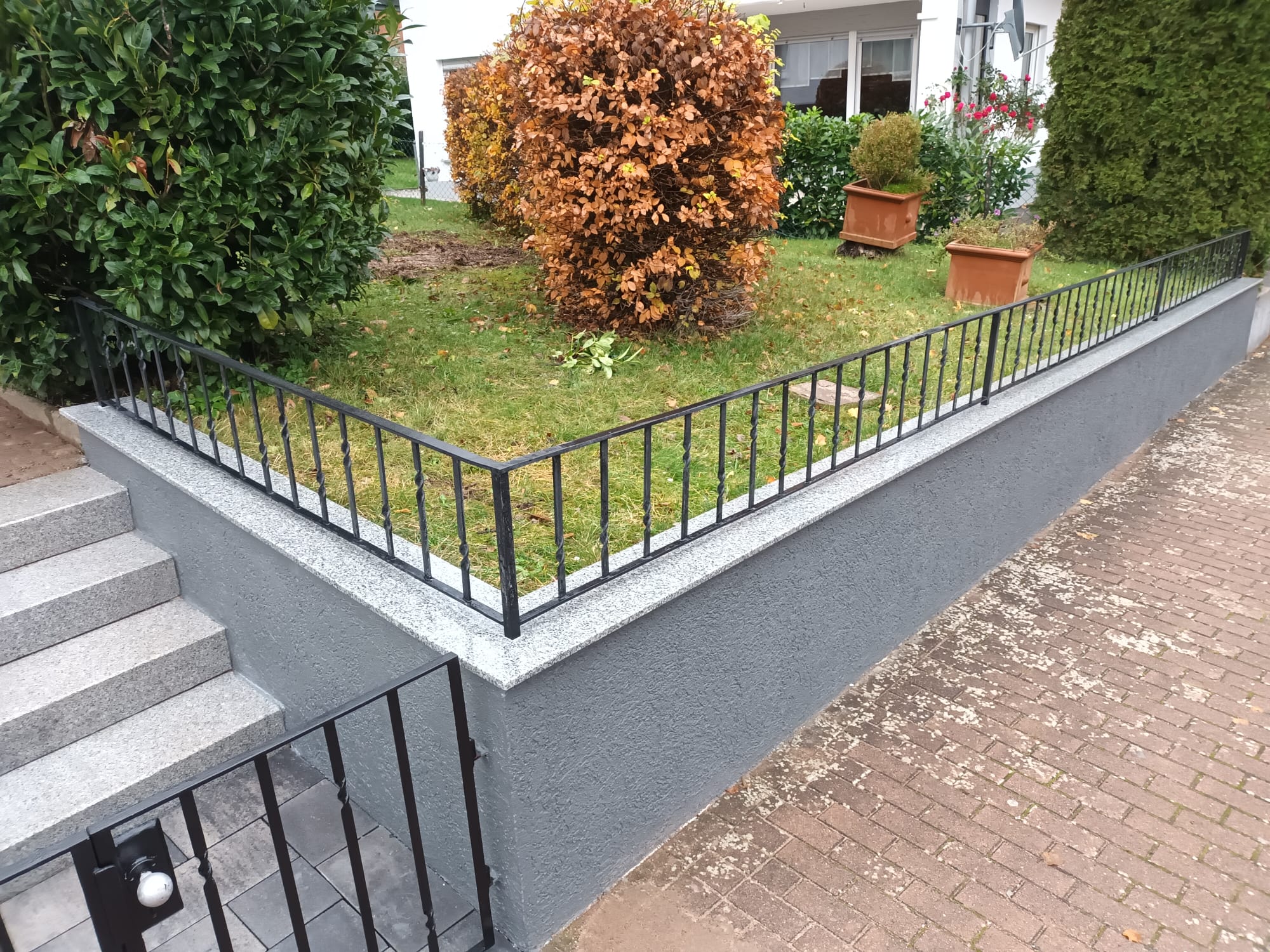 Niedrige Gartenmauer mit Klinkerabdeckung und Metallgeländer entlang eines Hauseingangswegs