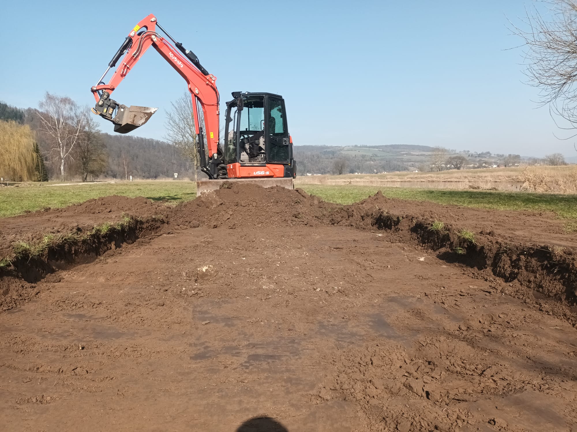 Kompaktbagger auf Schotterfläche in Einfahrt, Vorbereitung des Unterbaus vor Hausfassade