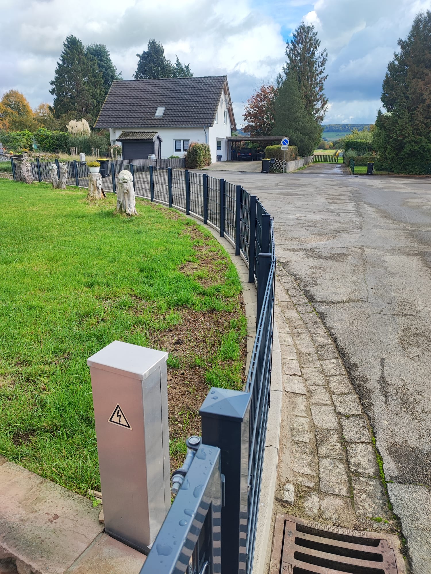 Schwarzer Metallzaun mit Schiebetor auf gepflasterter Einfahrt vor Gebäude