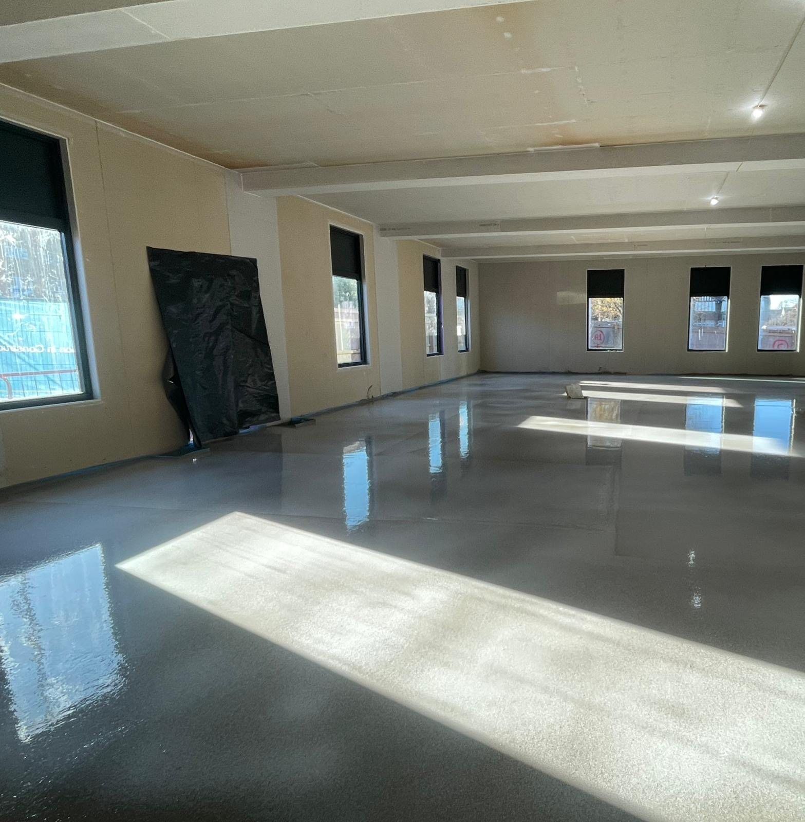 A large open floor of finished screed lit by a row of windows
